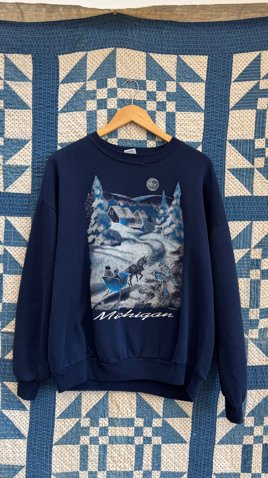 Navy blue sweatshirt with a graphic design on a hanger against a quilted fabric background